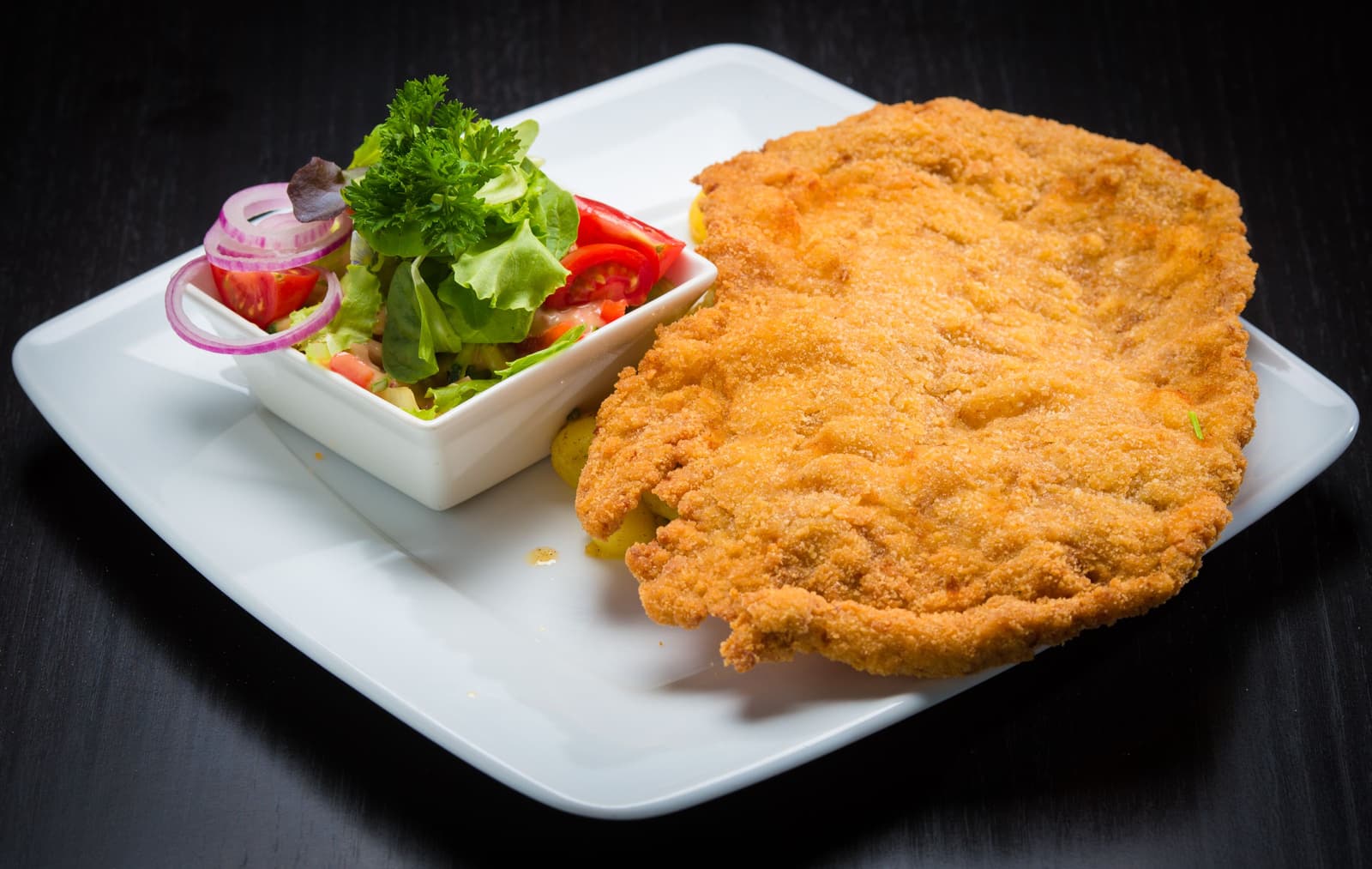 Una chuleta de ternera empanada y dorada servida con una ensalada fresca de tomate y lechuga