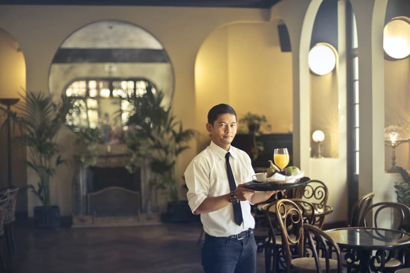 Un serveur porte un plateau avec des boissons et des fruits dans un restaurant élégant