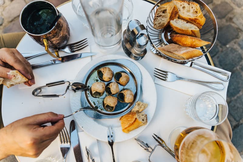 Caracoles, baguette en rebanadas y vino blanco en la mesa de una terraza de París