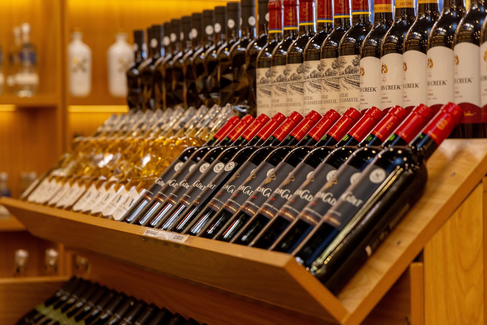 Rows of red and white wine bottles displayed on wooden shop shelving