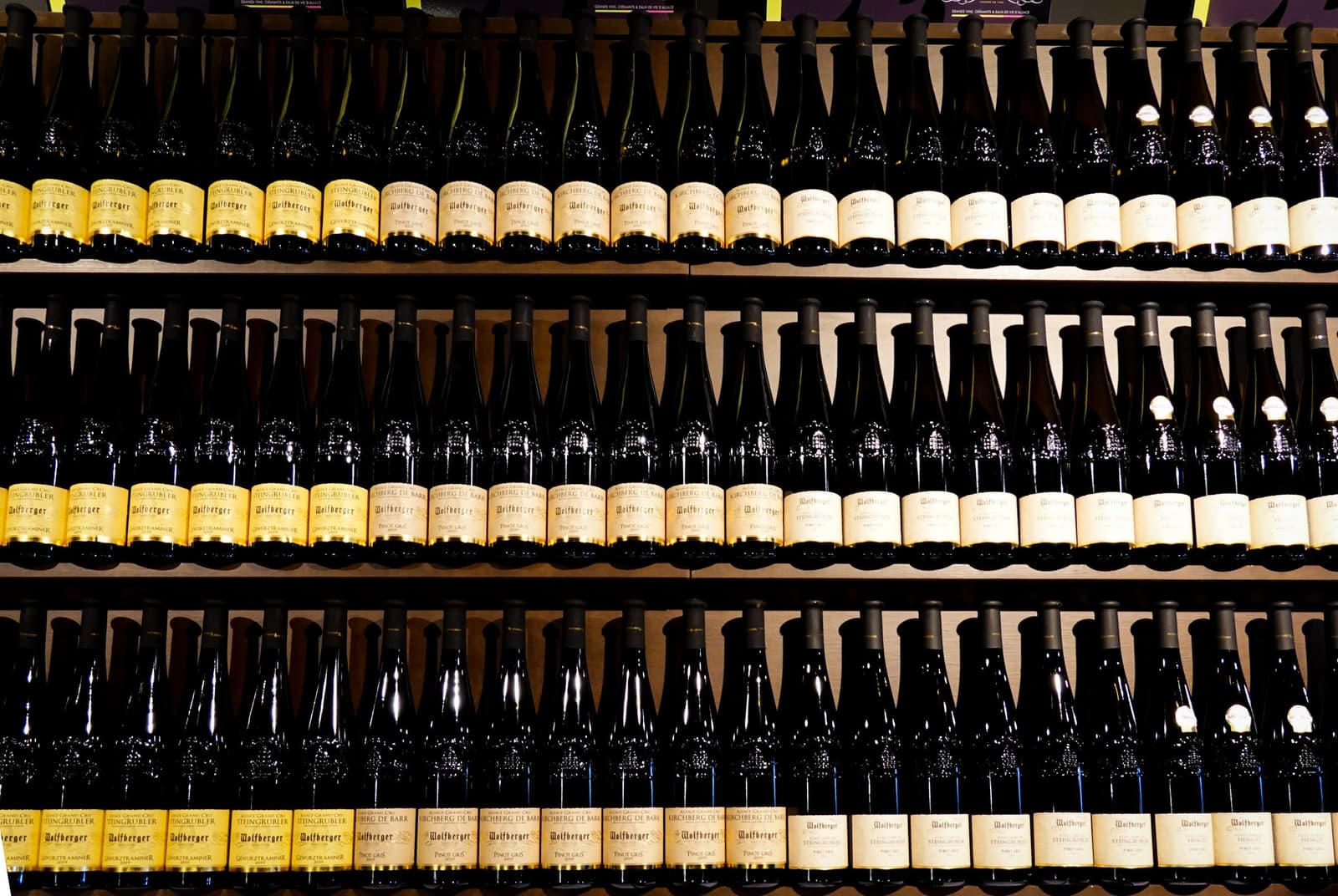 Three shelves of white wine bottles lined up in rows in a wine shop