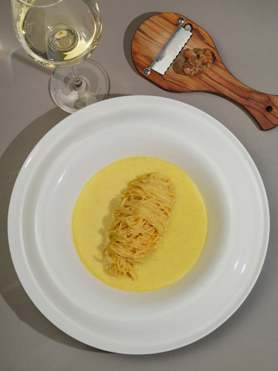 Frischer weißer Trüffel über Pasta gehobelt neben einem Glas Wein