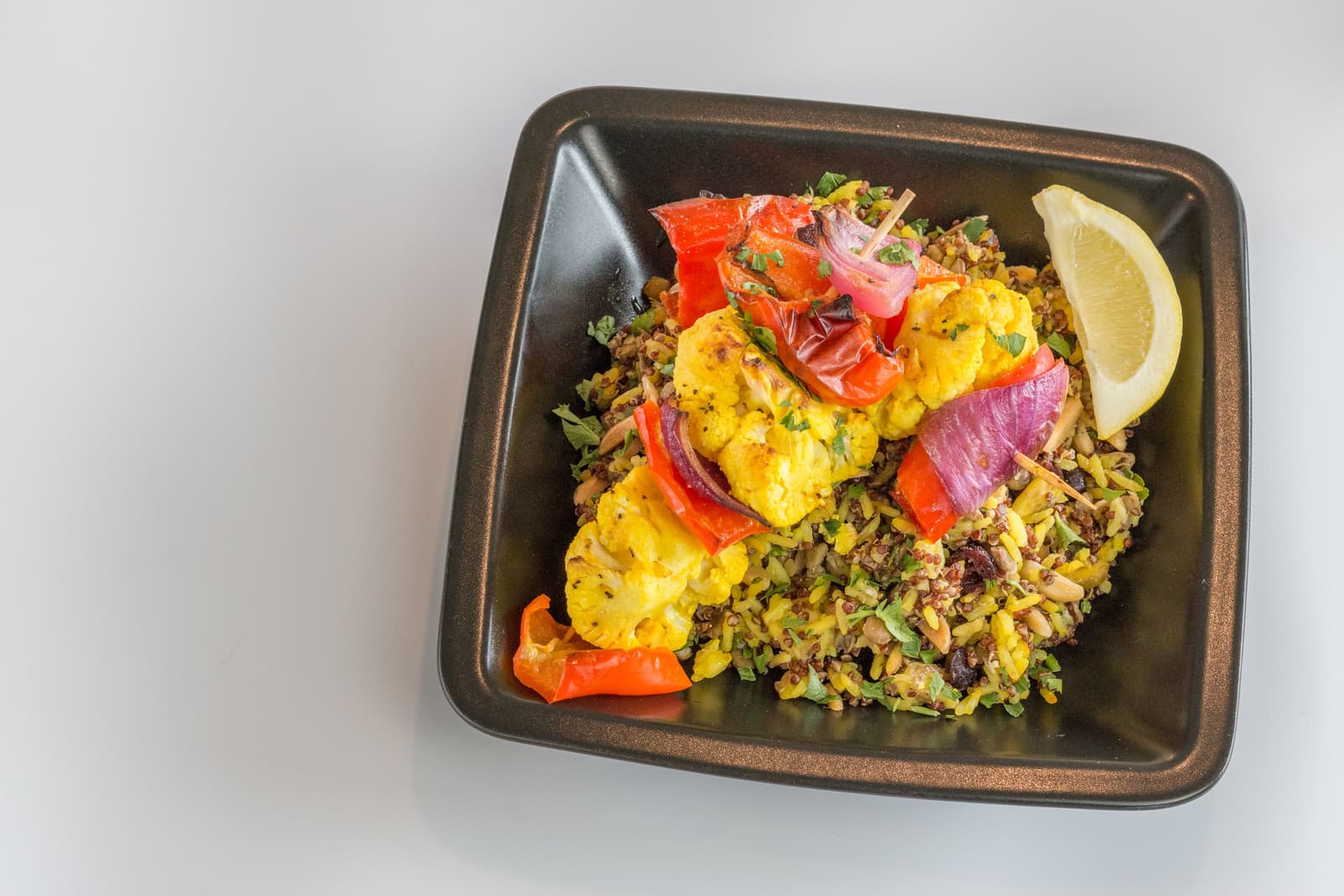 A bowl of spiced roasted cauliflower and potatoes topped with tahini, herbs and pomegranate seeds