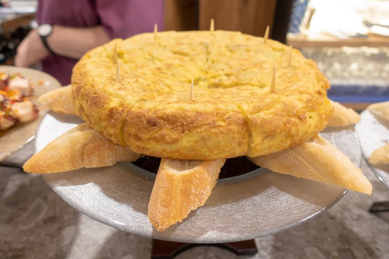 Tortilla de patatas intera tagliata a spicchi su fette di pane sul bancone
