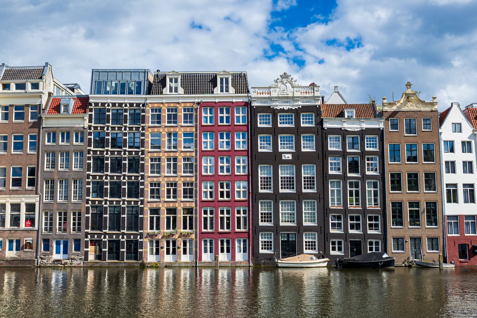 Rangée d'étroites maisons de brique aux fenêtres blanches reflétées dans un canal d'Amsterdam