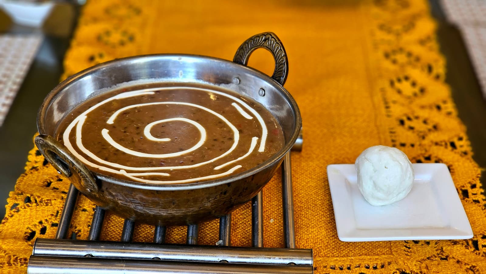 Bol de black daal crémeux nappé de crème, servi avec du pain naan