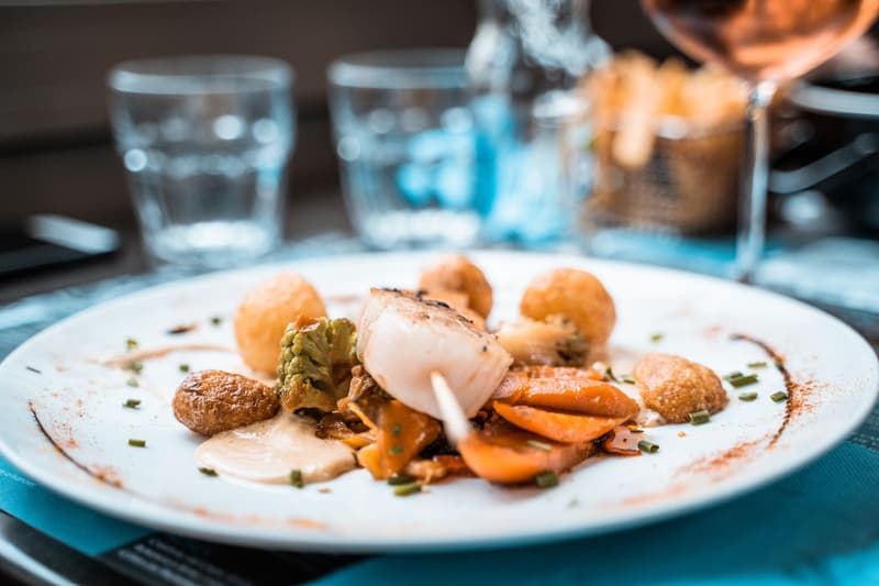 Gebakken sint-jakobsschelp met geroosterde groenten en krokante aardappelballetjes op een restauranttafel