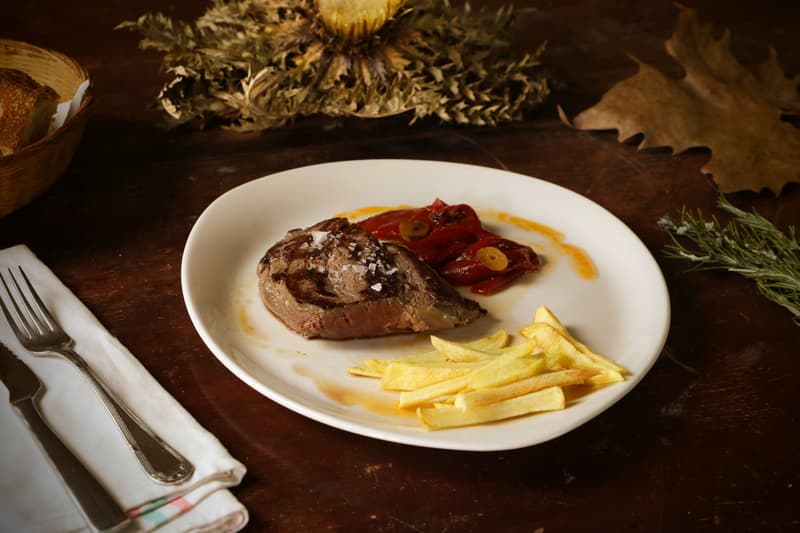 Grilled steak with roasted peppers and fries on a white plate