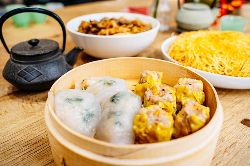 Dim sum al vapore, noodles e set da tè su un tavolo in legno