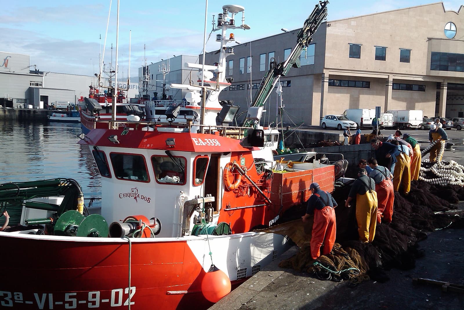 Red fishing boat moored in Vigo's port while crew sort nets on the quay