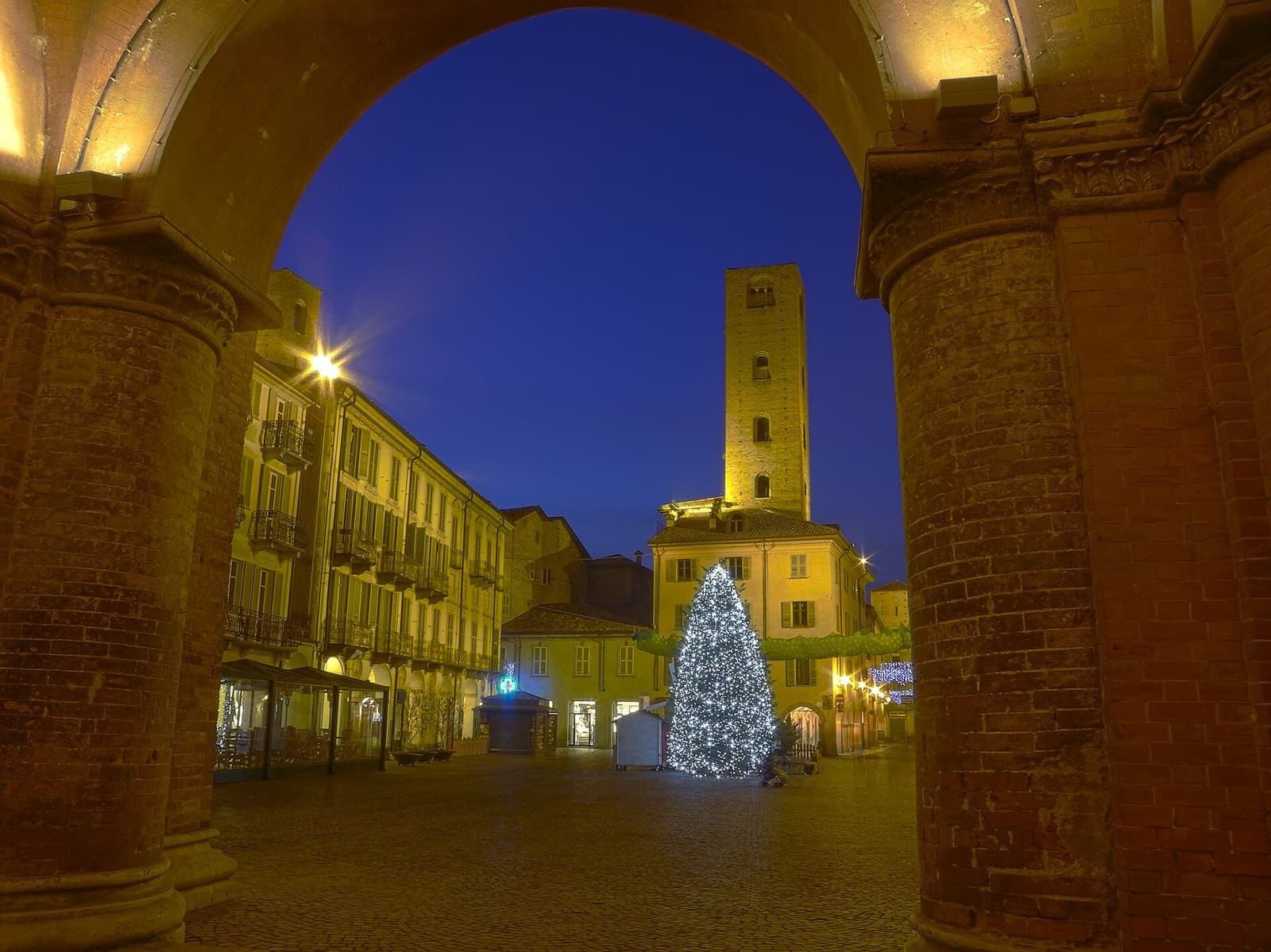 Piazza Risorgimento de Alba al anochecer, vista bajo el arco del pórtico catedralicio