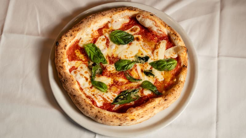 Napolitaanse pizza margherita met basilicum en gesmolten mozzarella op een wit bord en tafelkleed