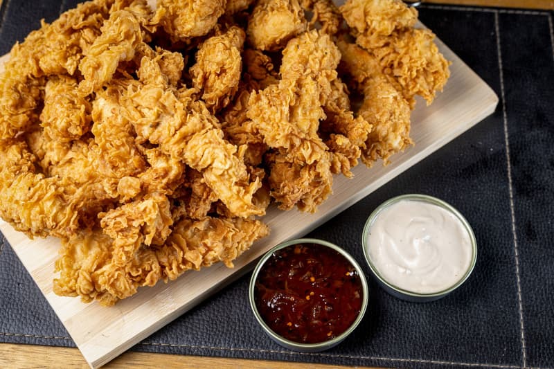 Tenders de poulet frit pané à la main sur une planche en bois avec deux sauces