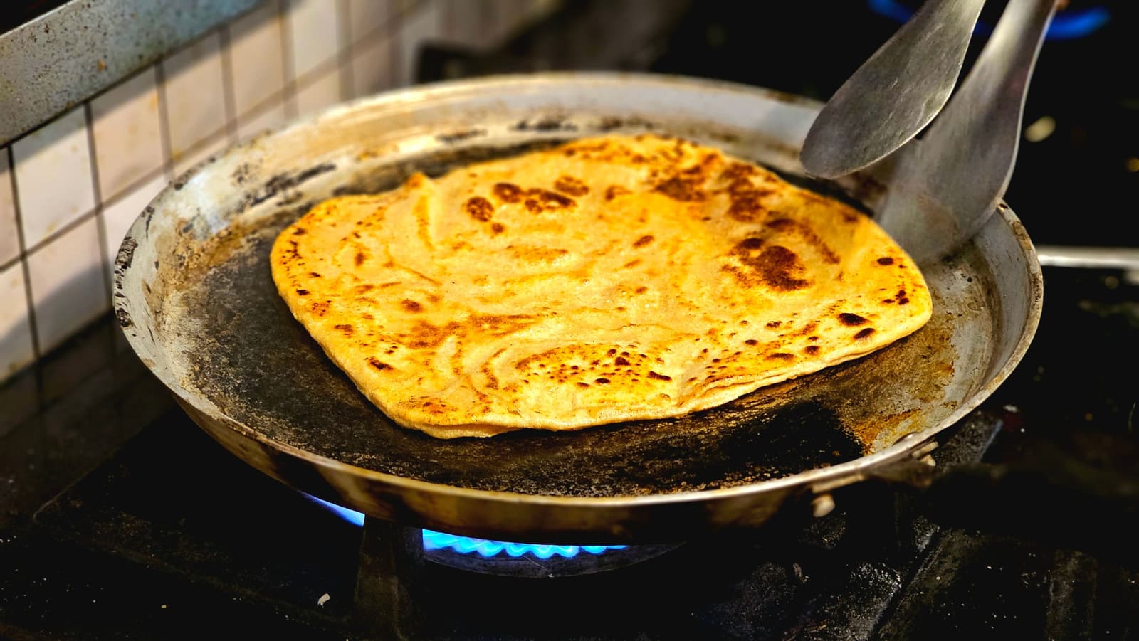 A golden roti canai flatbread being cut and plated in the kitchen