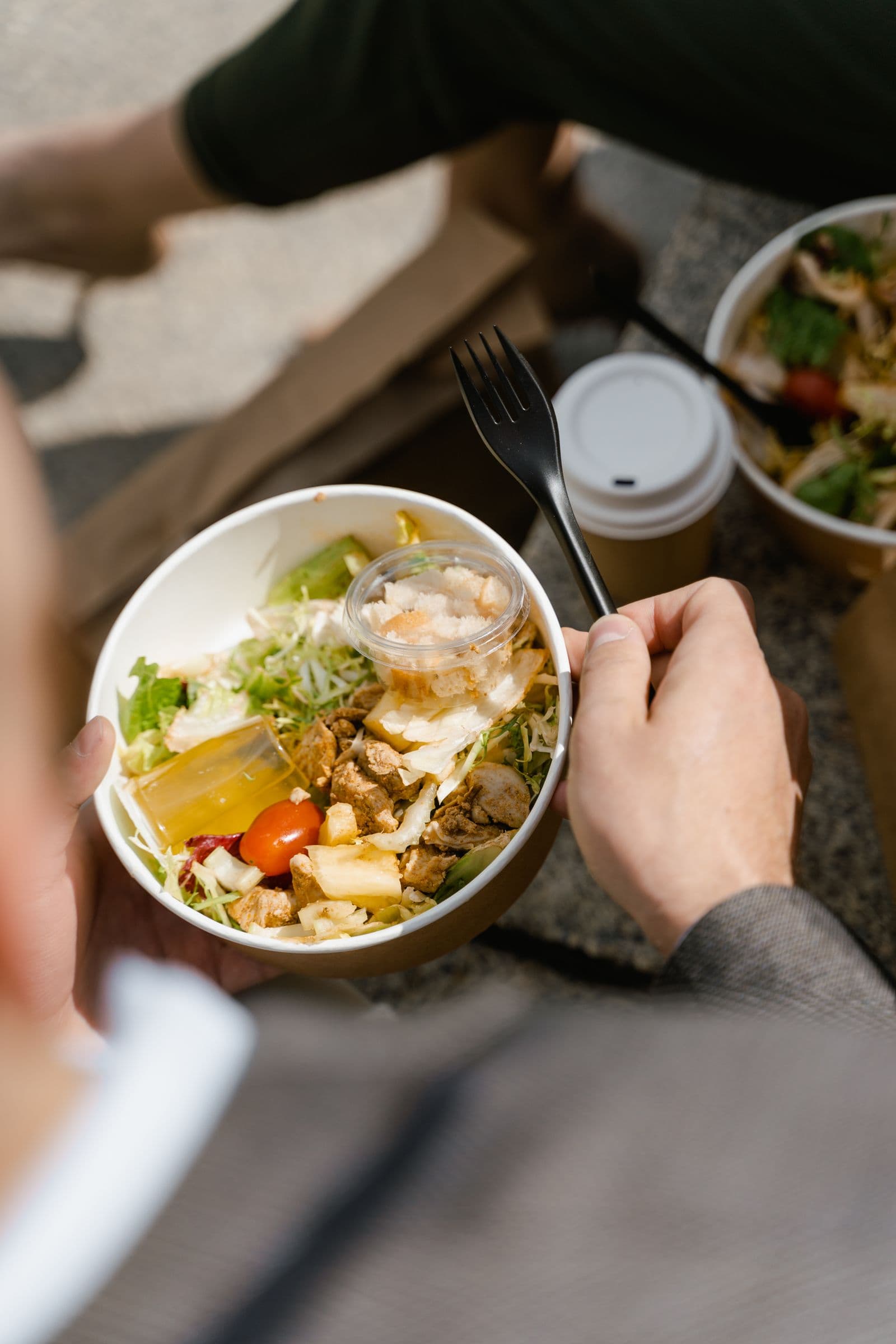 Personne tenant un bol de salade à emporter avec poulet, tomate et sauce