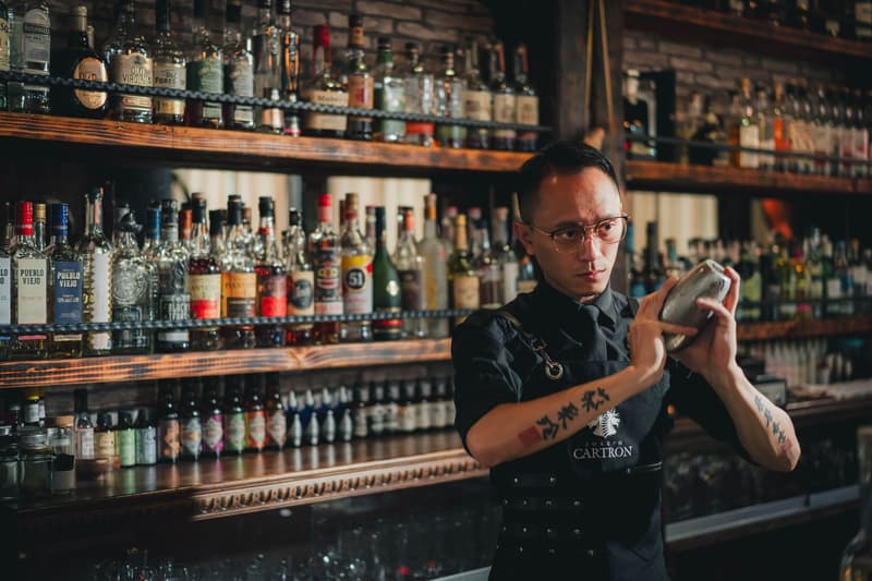 Barman schudt een cocktailshaker voor een verlichte muur met flessen