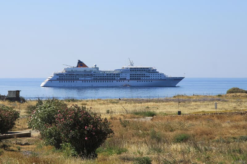 Weißes Kreuzfahrtschiff MS Europa vor Anker vor einer trockenen Küste mit Oleanderbüschen