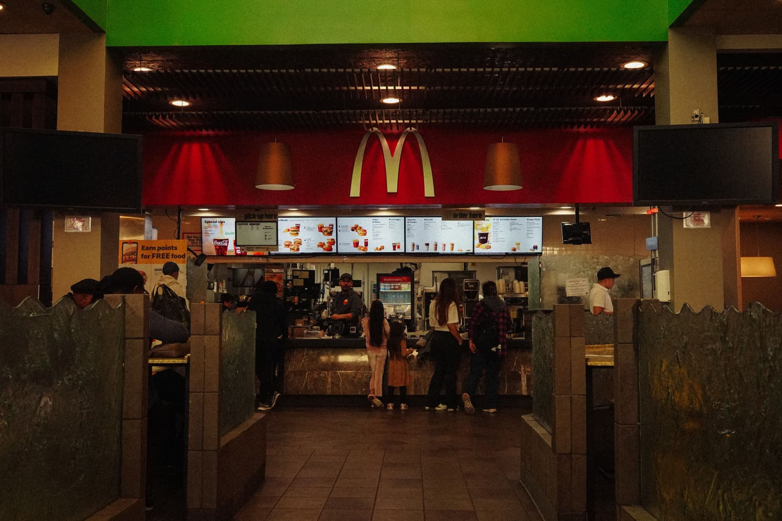 Clients faisant la queue au comptoir d'un fast-food sous des écrans menu