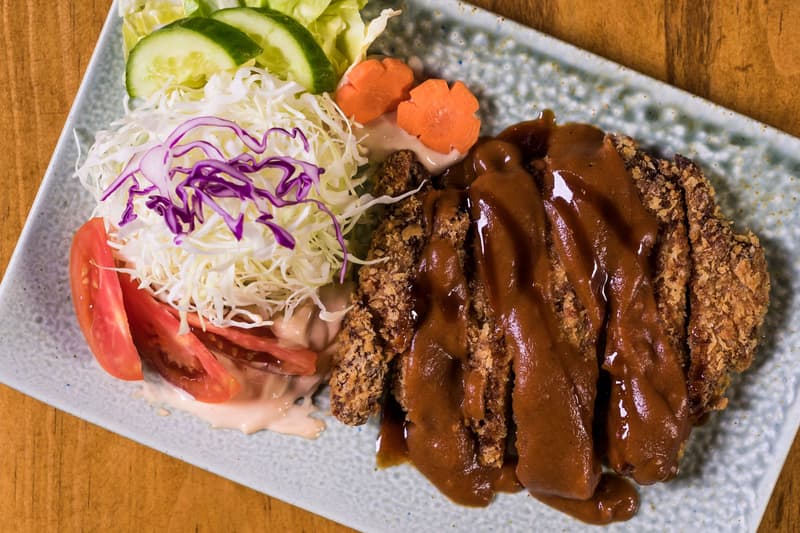 Vista cenital de una chuleta de cerdo tonkatsu empanada con salsa, col y tomate