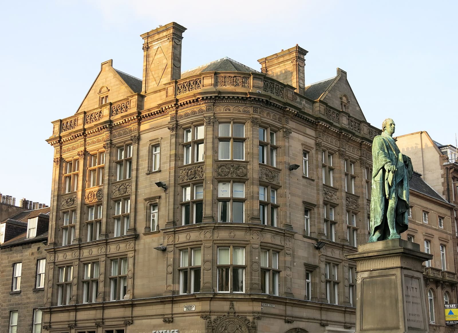 Victoriaans hoekpand van zandsteen aan George Street in Edinburgh naast een bronzen standbeeld
