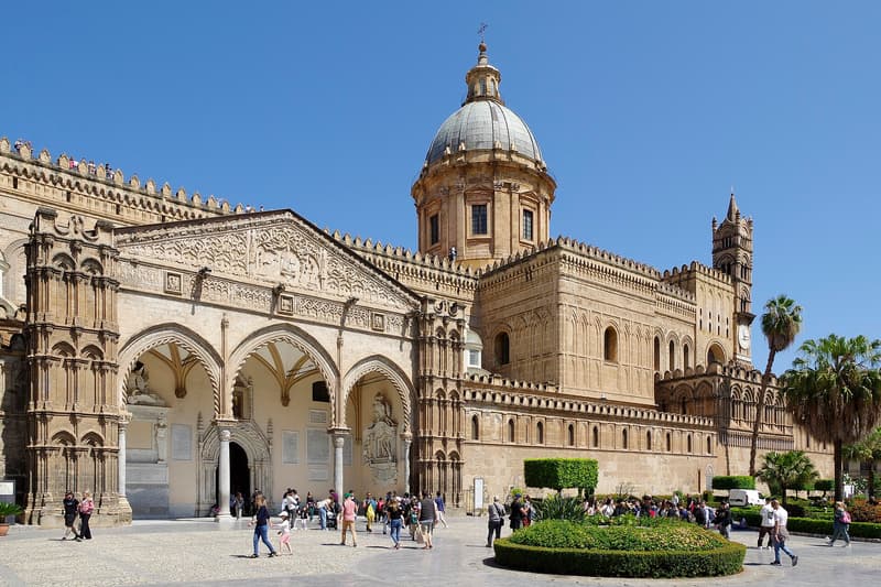 La cathédrale de Palerme vue depuis son parvis, avec le portique gothique, la coupole et des palmiers sous un ciel dégagé