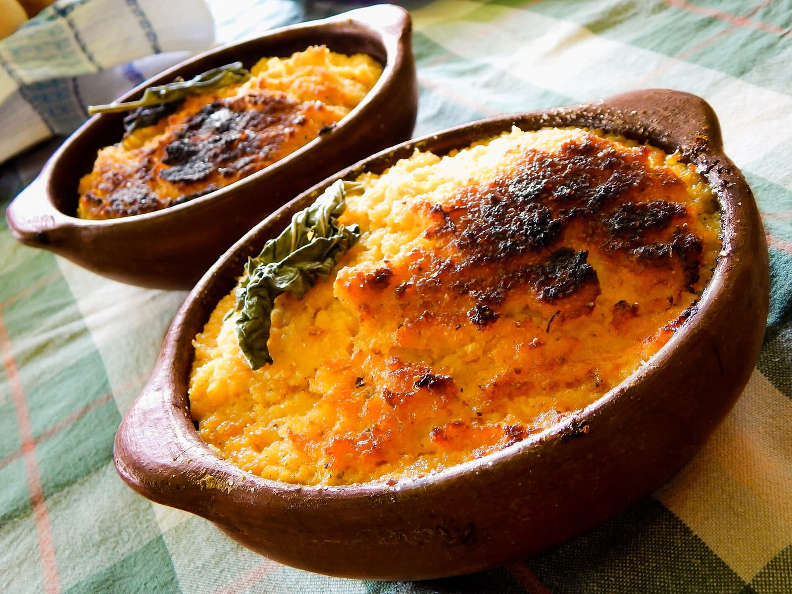 Two clay bowls of pastel de choclo with a browned corn crust and basil leaves