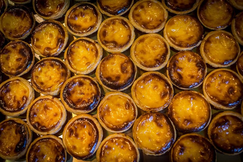 Filas de pastéis de nata recién horneados con manchas oscuras ampolladas sobre la crema vistos desde arriba