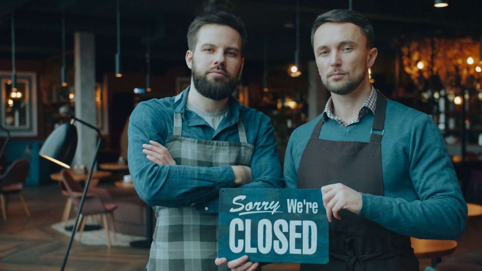 Twee restaurantmedewerkers met schort houden een gesloten-bordje vast