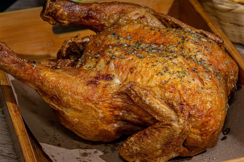 Poulet rôti entier à la peau dorée, parsemé d’herbes séchées, dans un plateau en bois