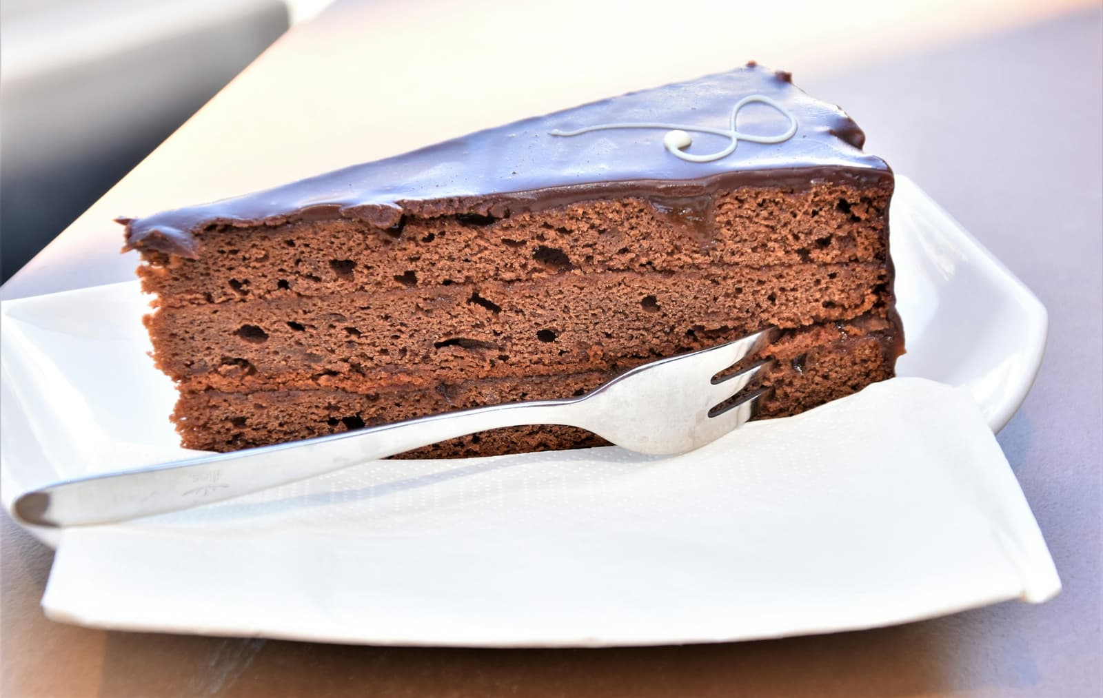 Part de Sachertorte au glaçage chocolat brillant et une fourchette sur une assiette blanche