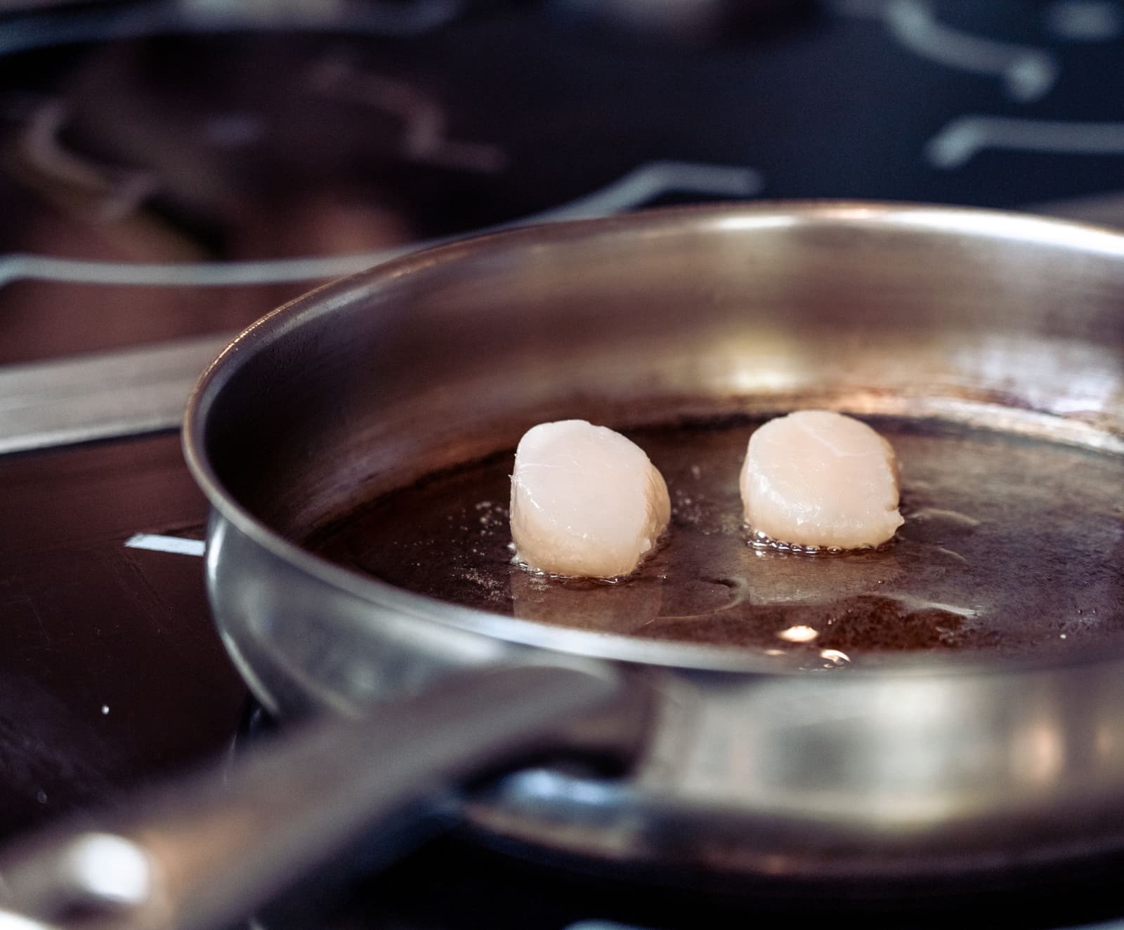 Deux noix de Saint-Jacques saisies dans une poêle en inox avec du beurre noisette