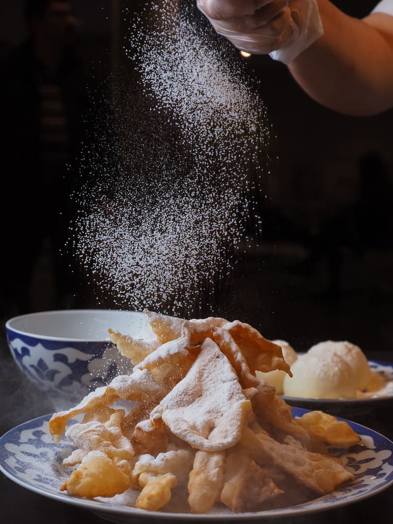 Puderzucker wird über aufgeblähtes süßes Frittiergebäck gestreut