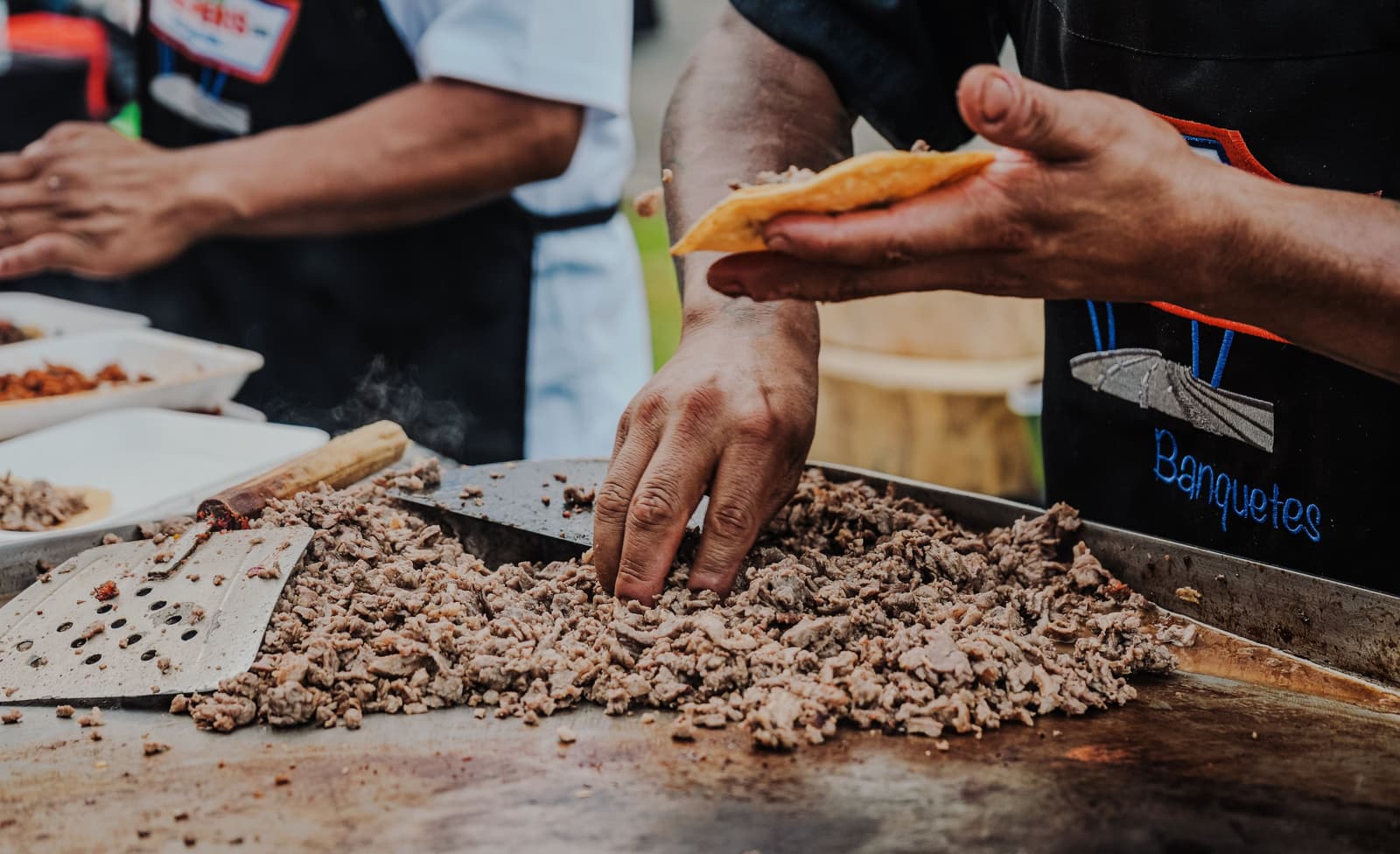 Street food vendor chopping grilled meat on a flat-top griddle for tacos