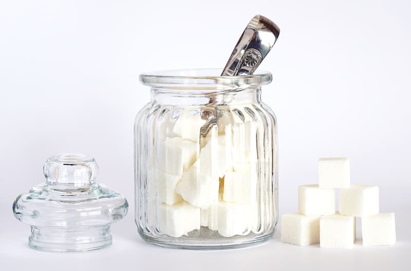 Morceaux de sucre blanc empilés près d'un bocal en verre et d'une pince argentée
