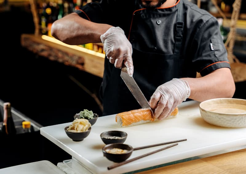Un chef en tenue noire tranche du poisson sur une planche avec un long couteau