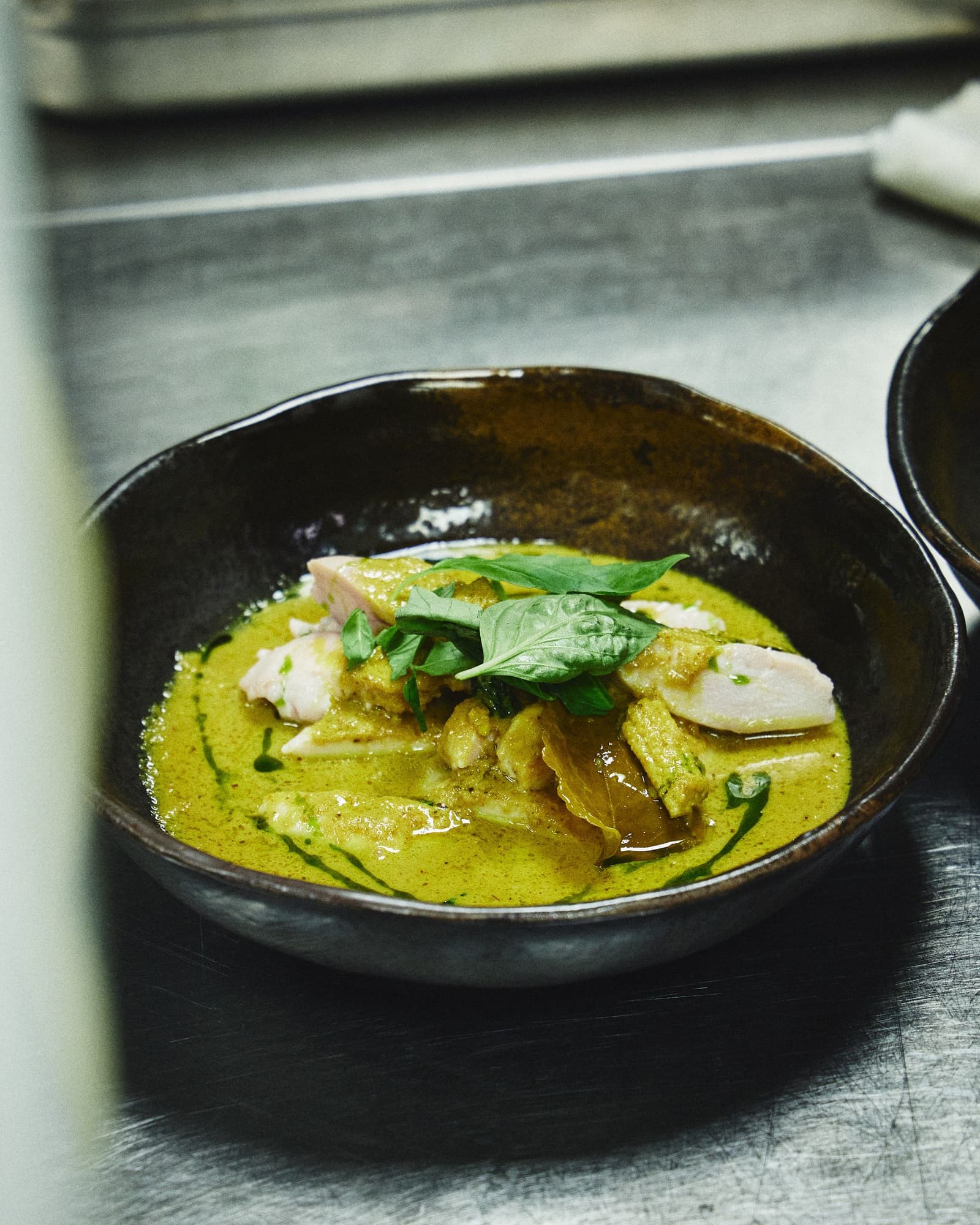 A dark bowl of Thai green curry topped with fresh basil leaves