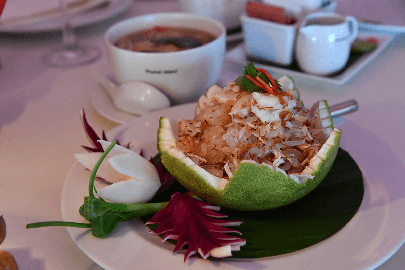 Ensalada de pomelo tailandesa con gambas, cangrejo y coco tostado en un plato blanco