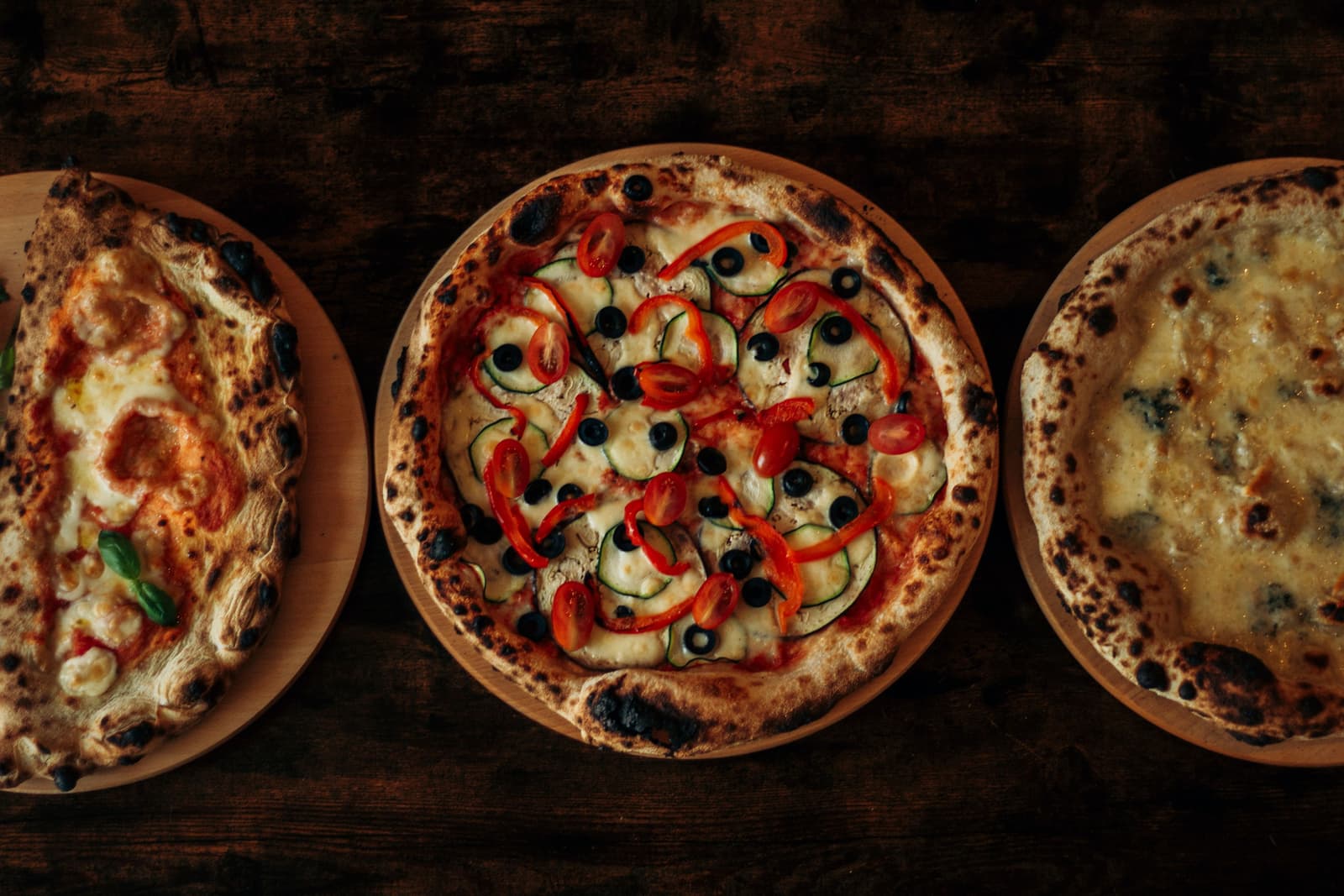 Pizzas napolitanas al horno de leña con la corteza tostada y abombada sobre una mesa oscura