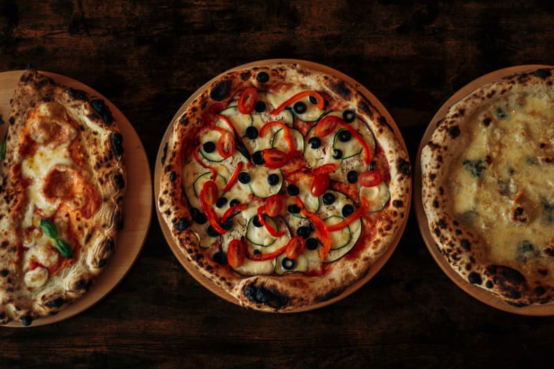 Im Holzofen gebackene neapolitanische Pizzen mit angekohltem, blasigem Rand auf einem dunklen Holztisch