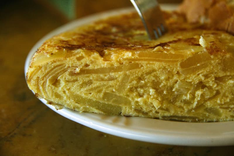 Part de tortilla de patatas sur une assiette blanche, couches de pomme de terre visibles
