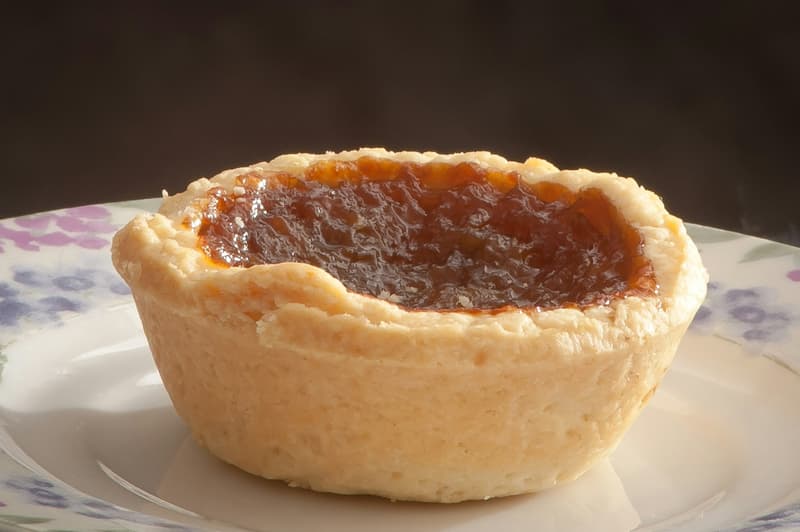 Un treacle tart individuale nel suo stampo di pasta con ripieno lucido di sciroppo dorato