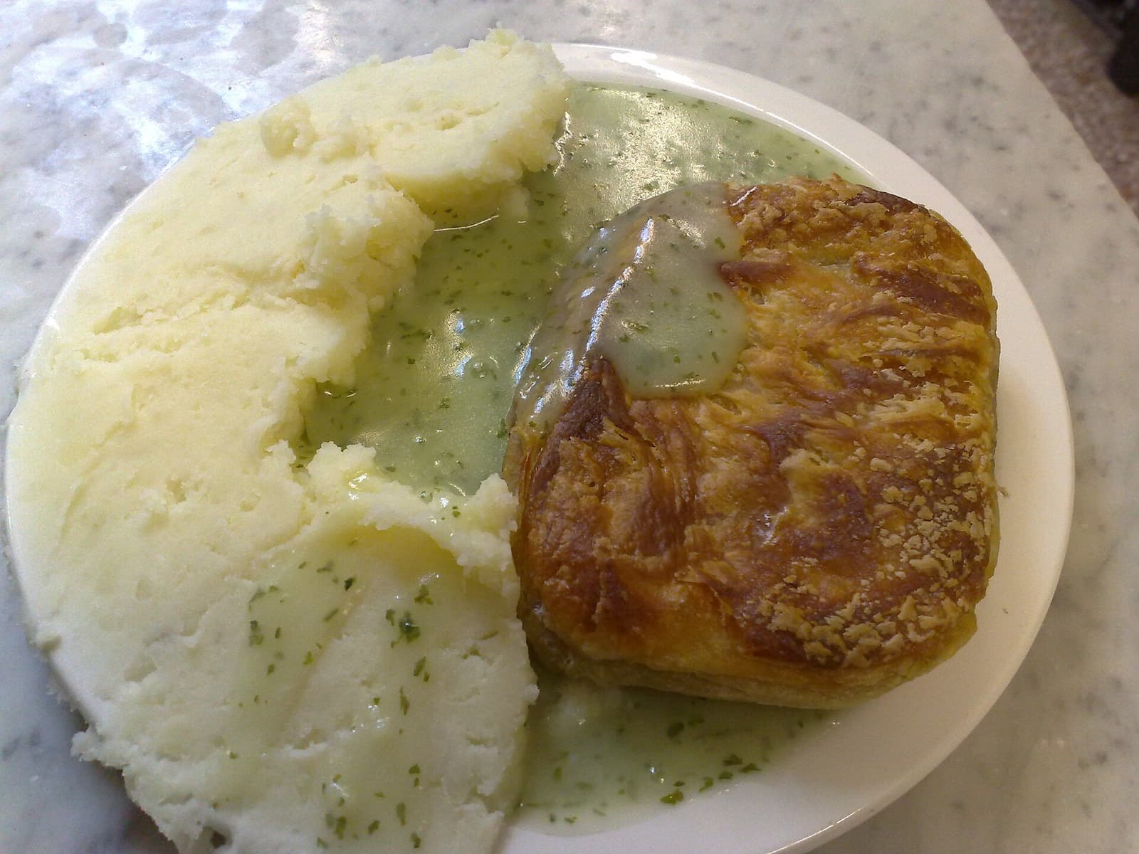 Pie, aardappelpuree en groene peterseliesaus op een bord bij M. Manze in Bermondsey